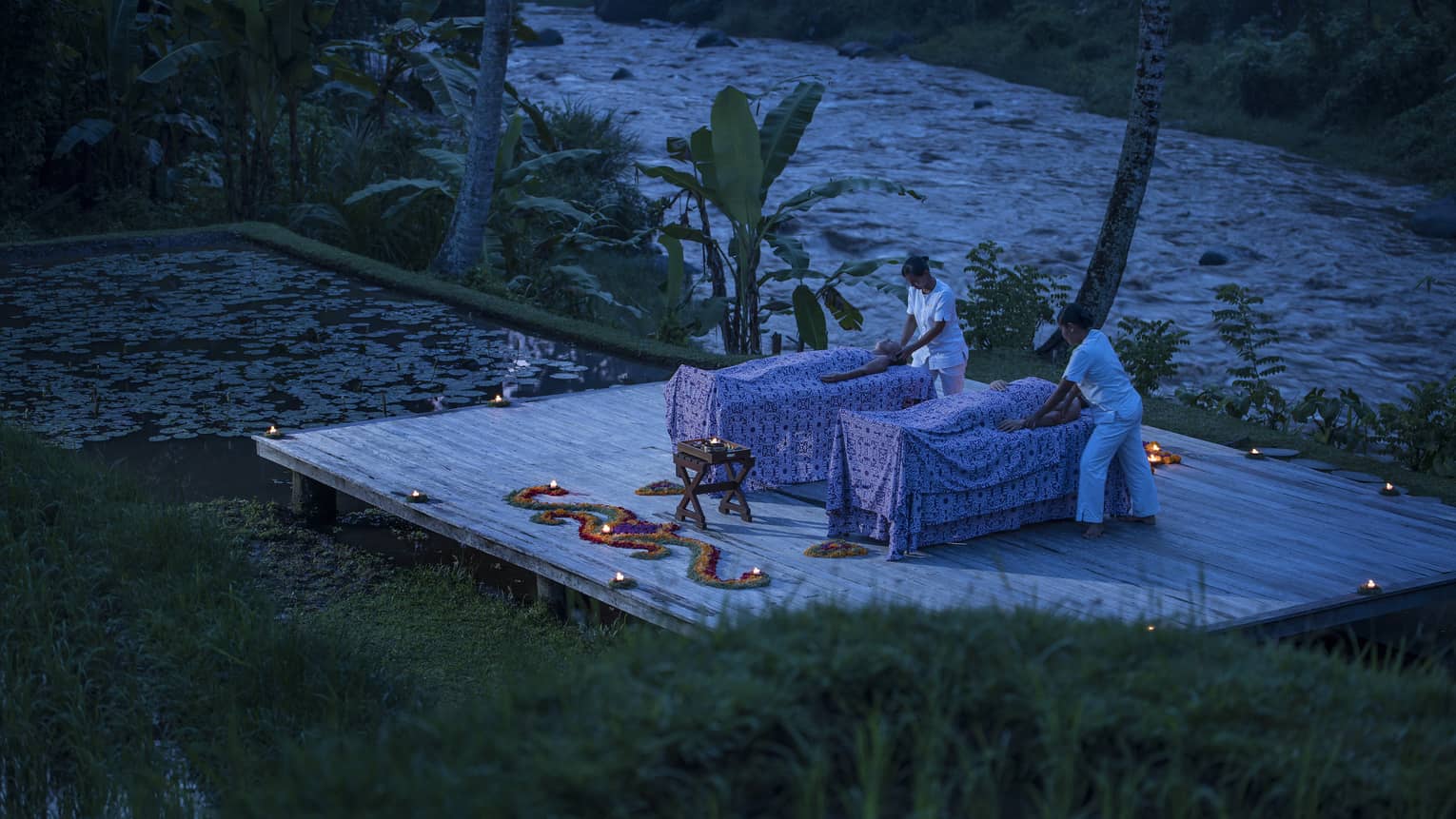 Two guests receive candle-lit massages on a dock at night 