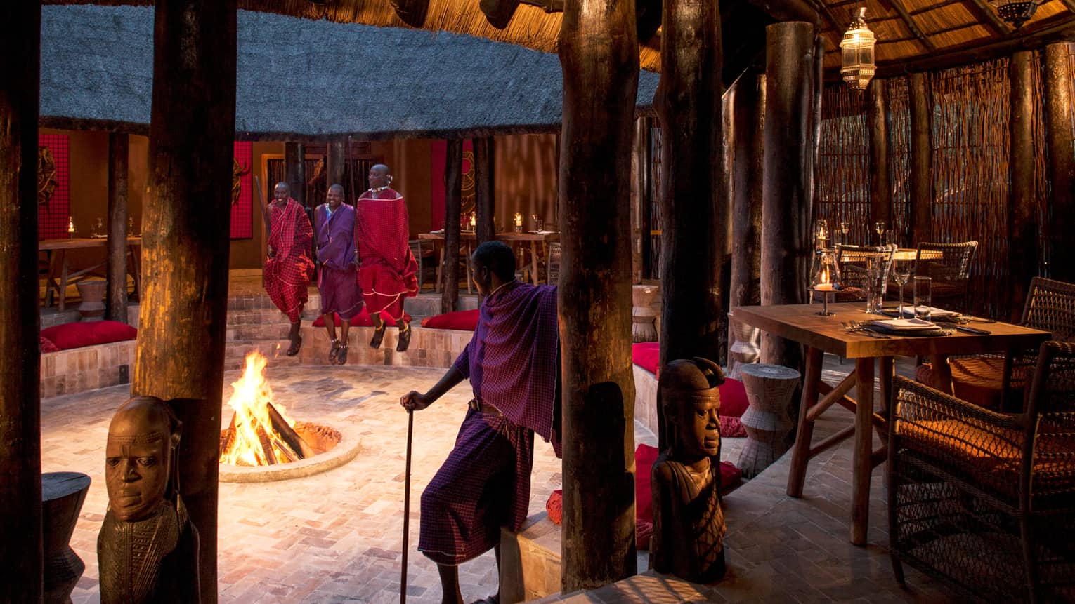 Maasai guides stand around open fire pit in middle of Boma Grill dining hut