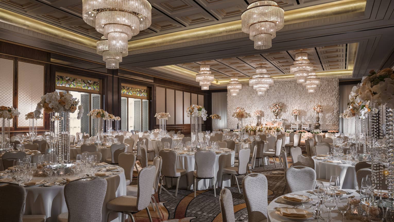Large crystal chandeliers hang over round banquet tables in ballroom