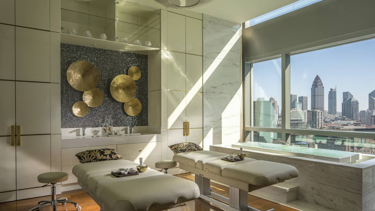 Couples massage beds with pillows under brass disc art on walls in L’Océan Spa