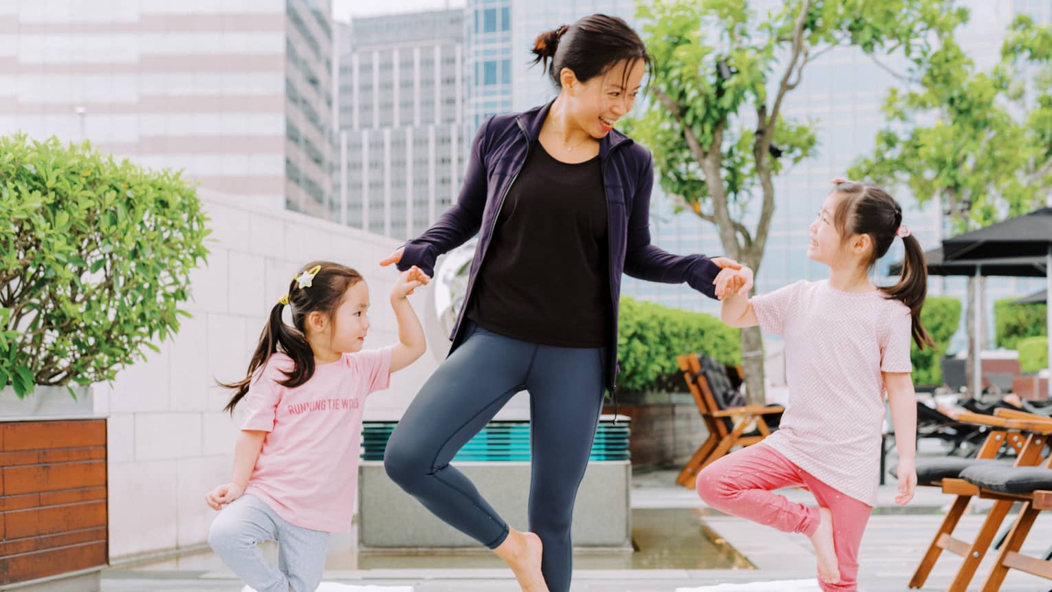 A mother and two young daughters laughing while doing yoga together.