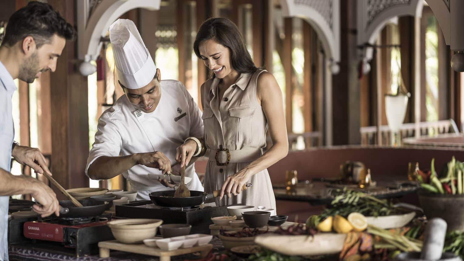 A chef is instructing a man and woman in the Ikan Ikan Cooking Class