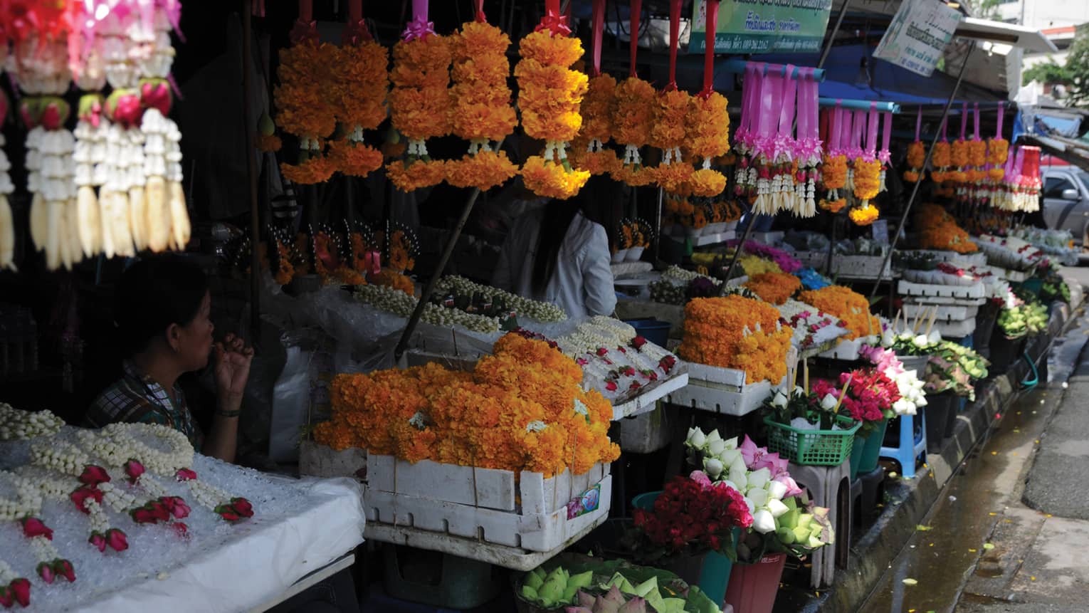 Displayed in an outdoor market, rows of traditional floral garlands and buckets of bouquets bursting with vibrant colour.