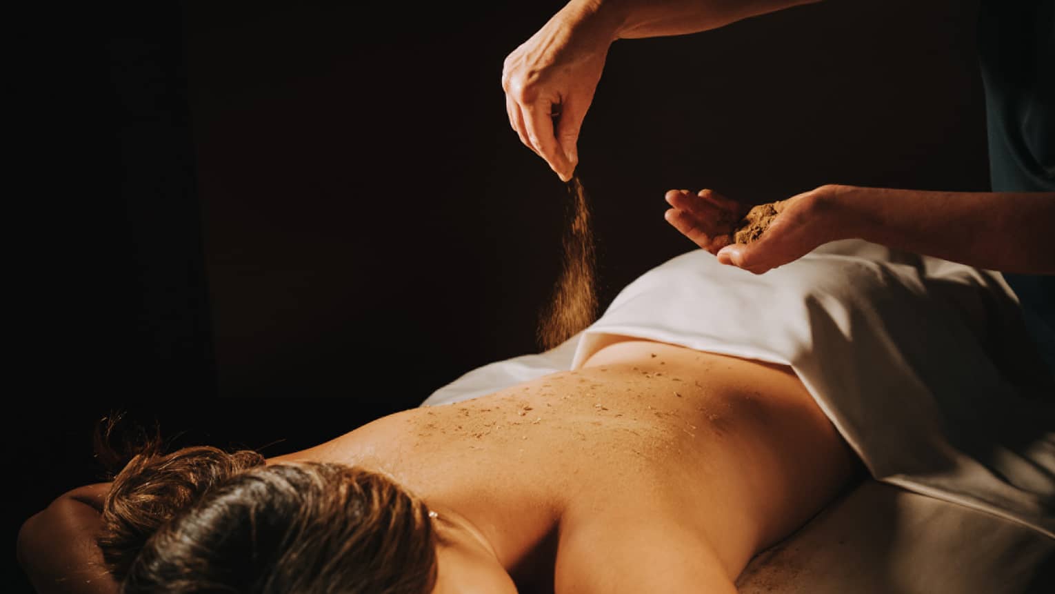 Spa staff sprinkled coffee powder over woman's bare back as she lays on massage table