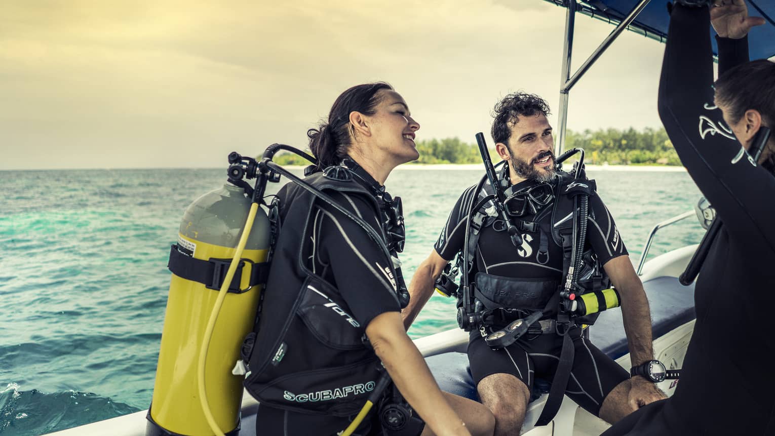 Diving instructor and couple wearing scuba gear sit at edge of boat