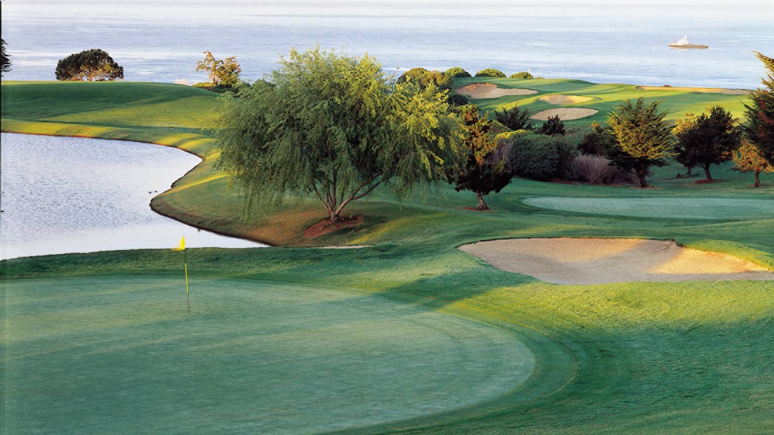 Golf course greens. sand trap, pond, ocean in background