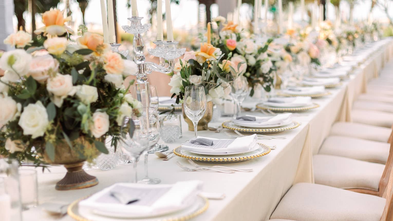 A long table with orange and cream flower centerpieces and set for a wedding.