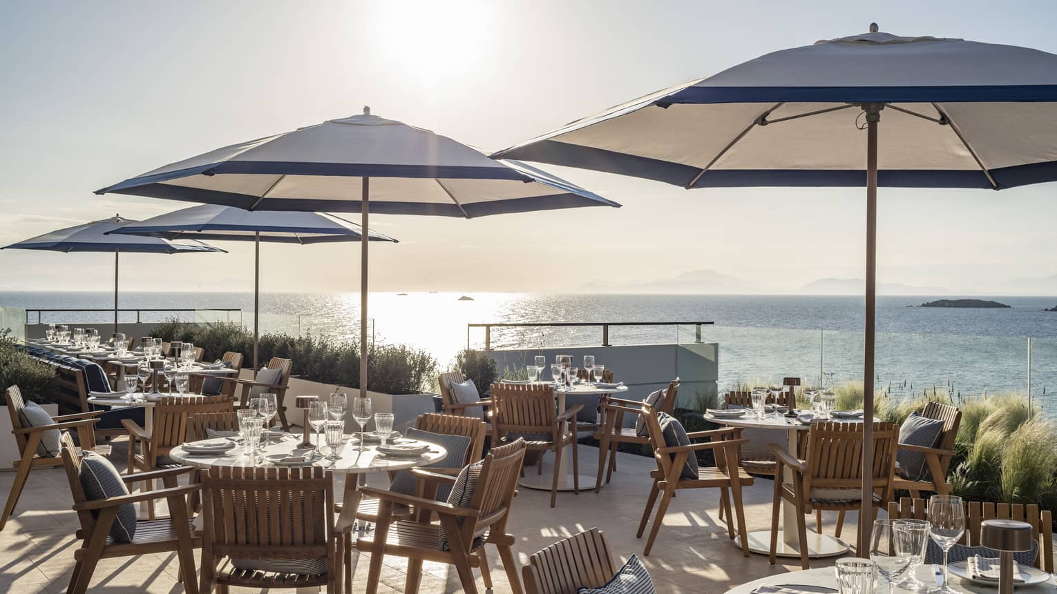 Sunny outdoor restaurant in Greece, blue umbrellas at wooden tables, overlooking the sea