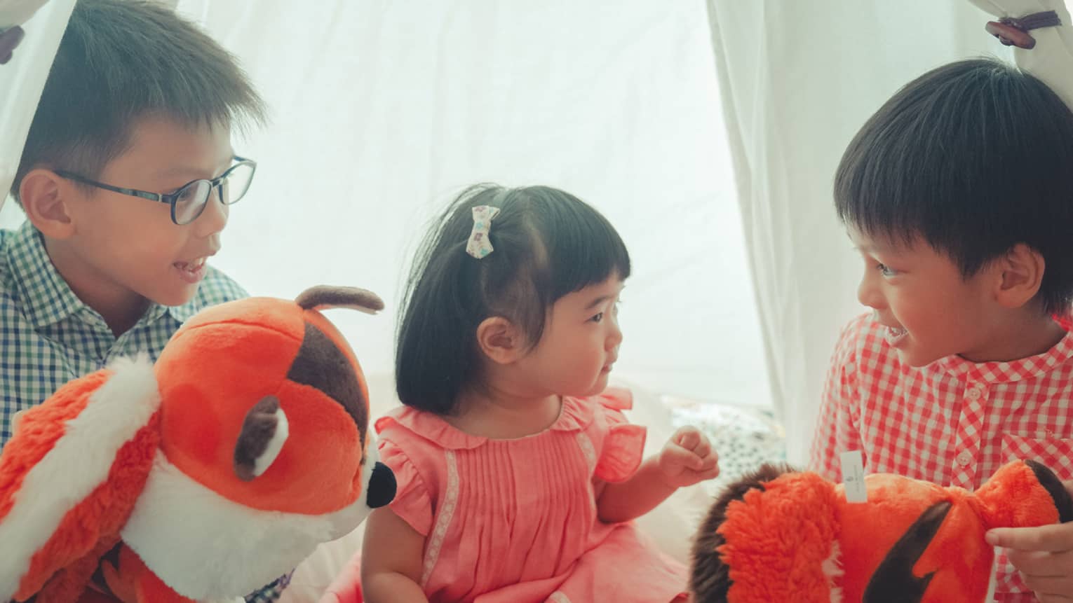 Three young children playing with stuffed animals under a tent.