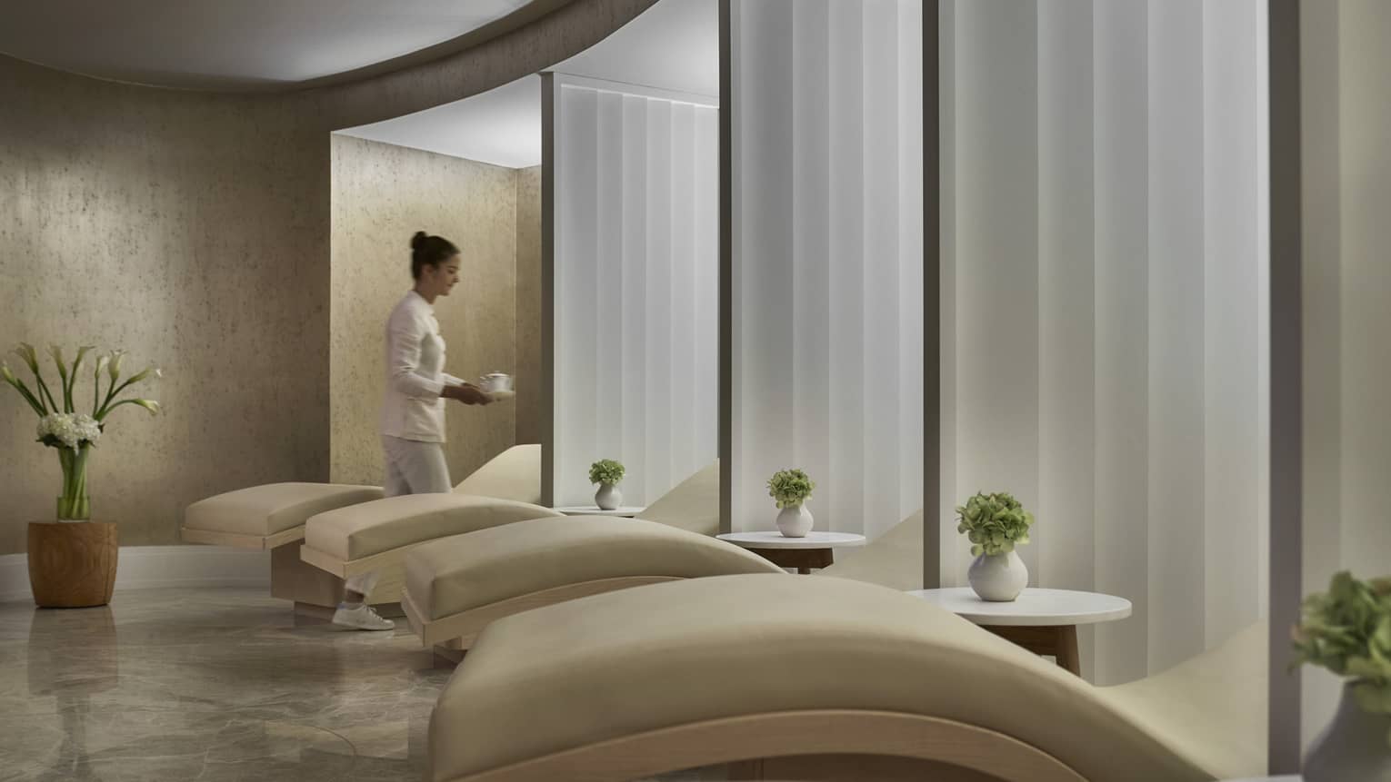 A woman caries cup of coffee in spa relaxation room with five lounge chairs