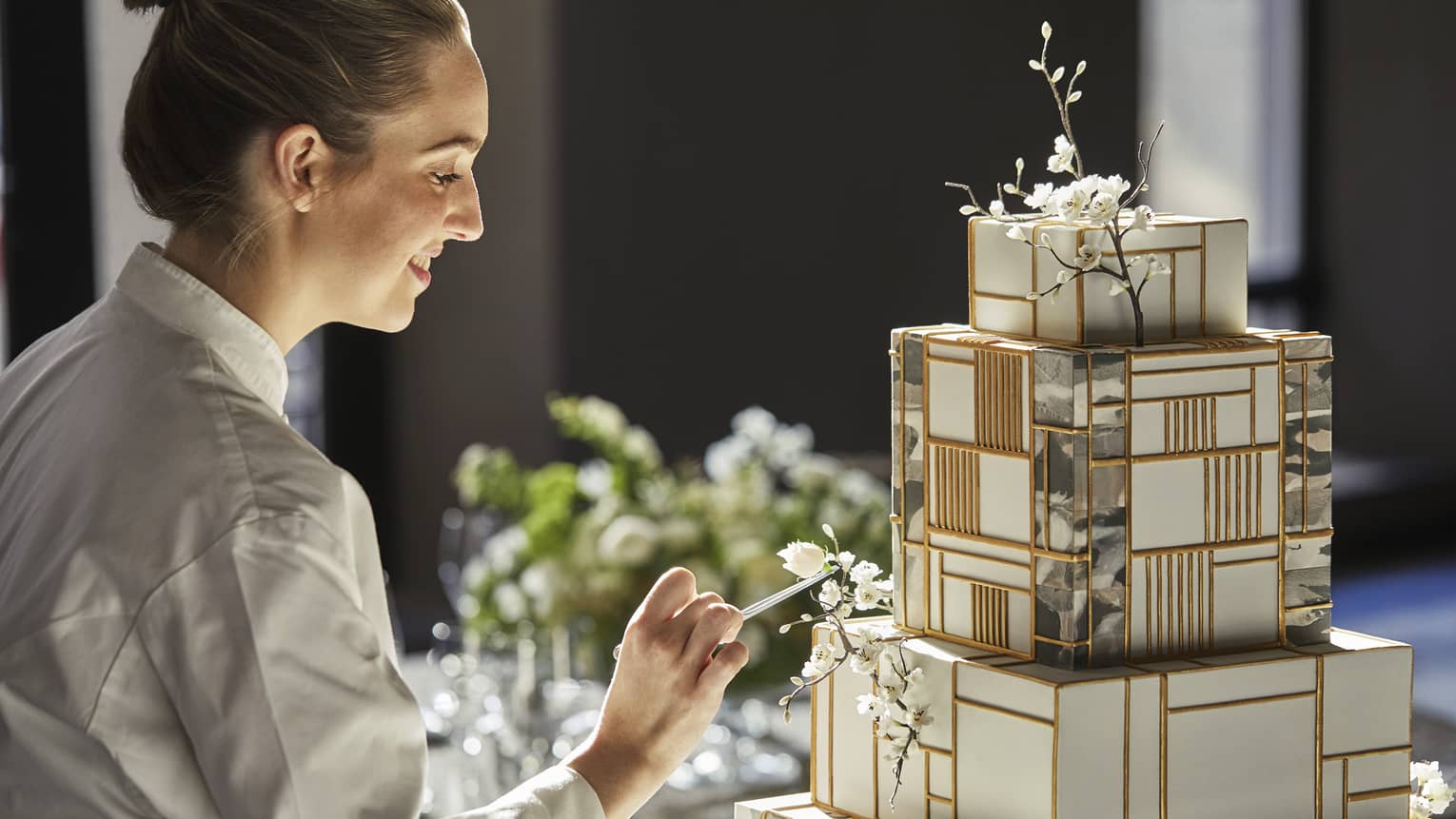 Pastry chef decorates elaborate tiered cake with gold accents