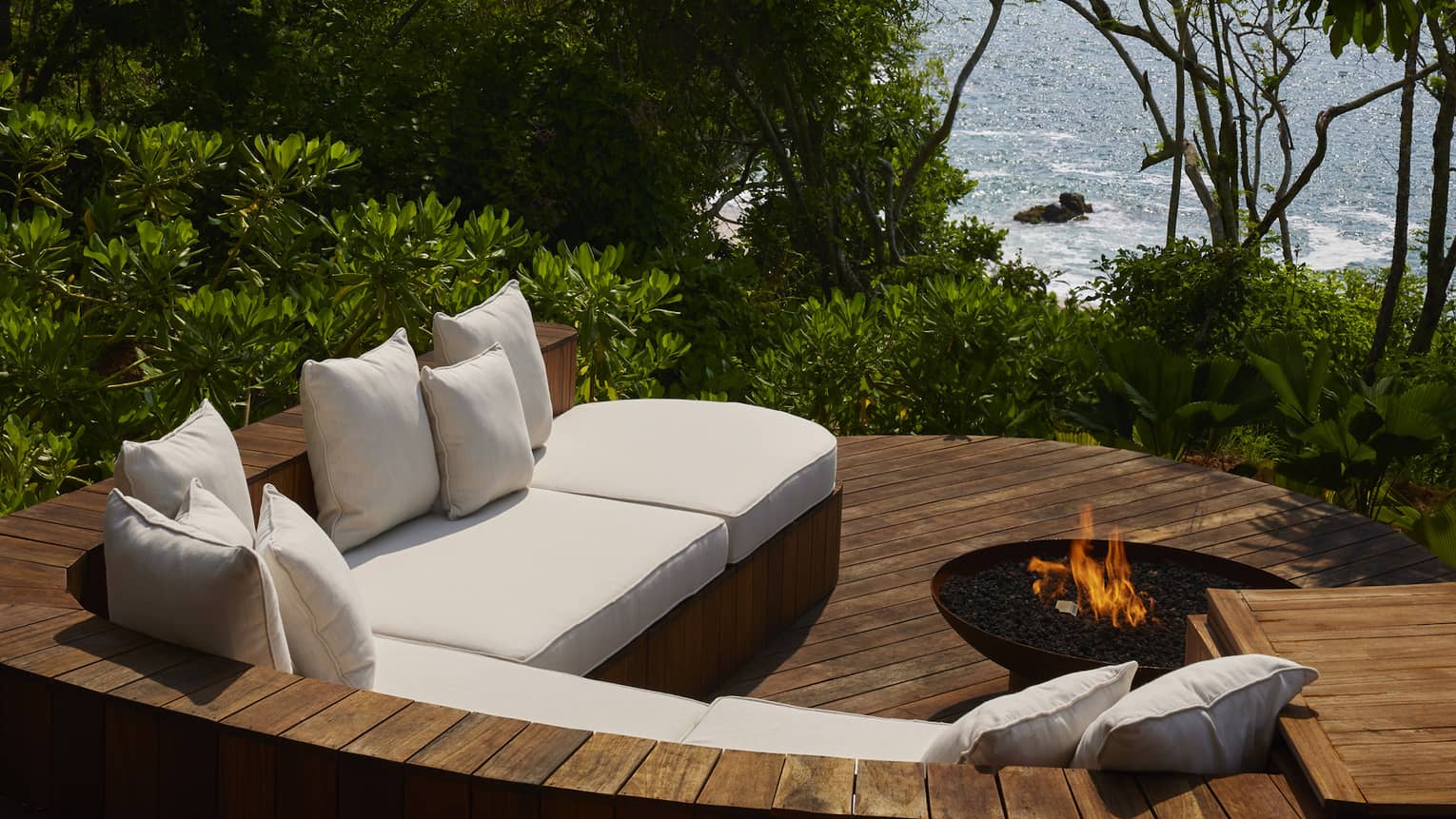 A sunken wooden patio with sofa and firepit, jungle and ocean view