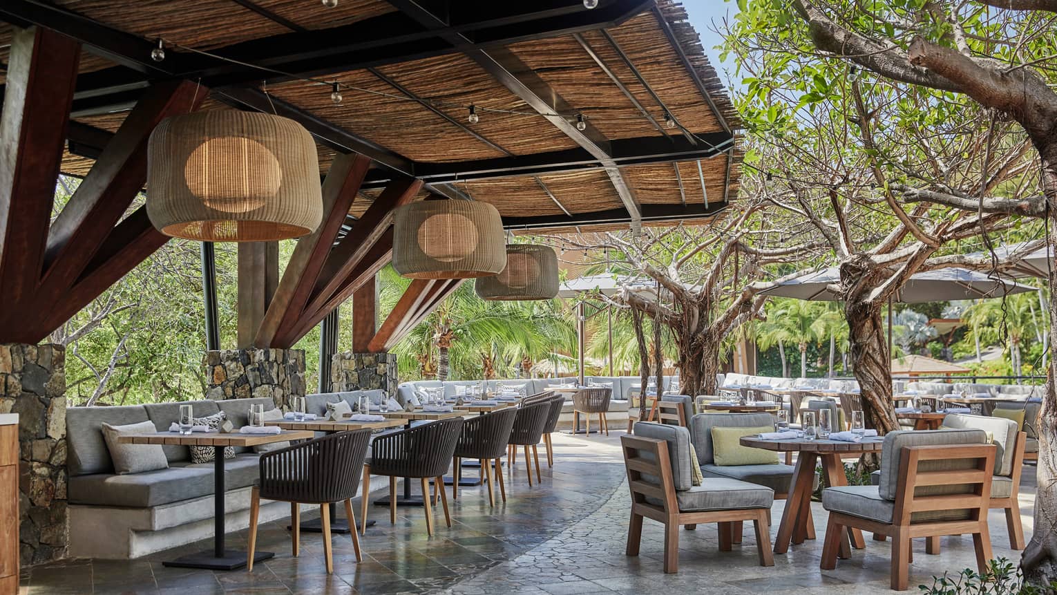 Bahia restaurant patio dining tables and chairs with thick grey cushions, large bamboo round lights hang from awning