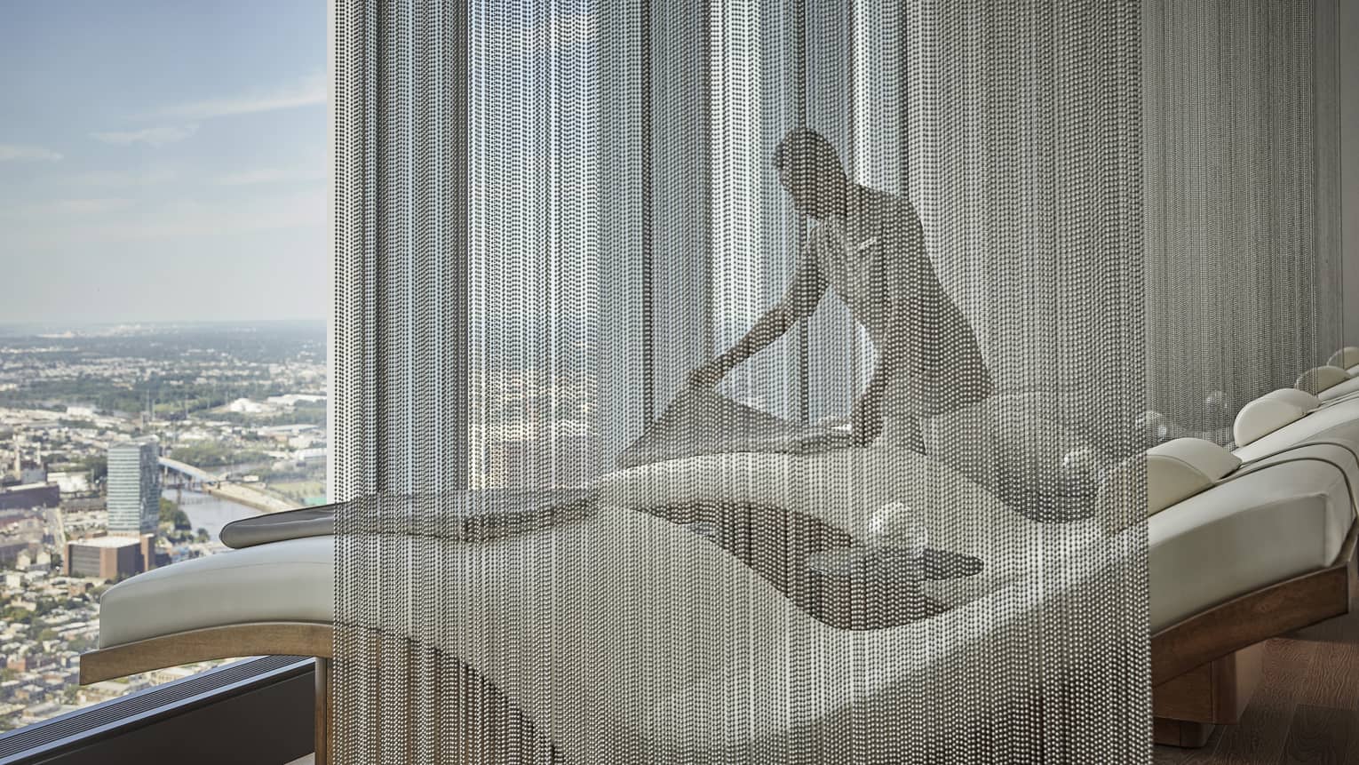A spa staff member organizing and getting a room ready for a treatment, a large window is looking out at a city.