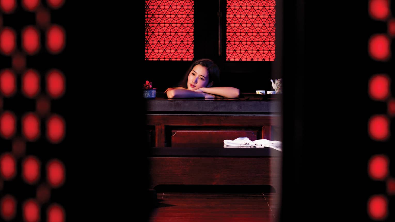 Woman rests head on crossed arms on table in dark red-and-black spa