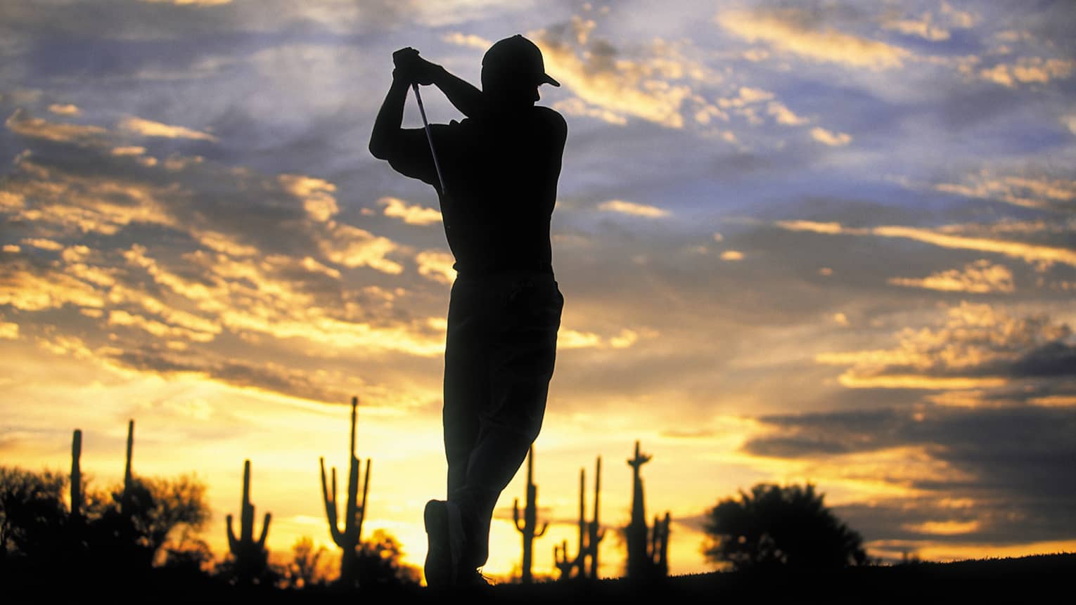 Silhouette of golfer swinging club against sunset sky at Troon North golf course