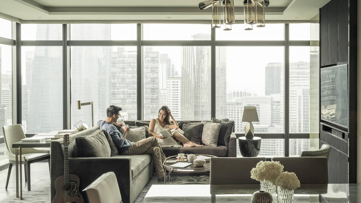 Couple relaxes on sofas in hotel suite with bright floor to ceiling windows