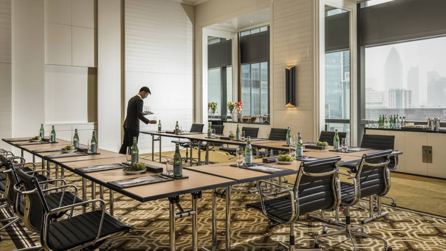 Hotel staff sets water glasses on modular meeting table near windows