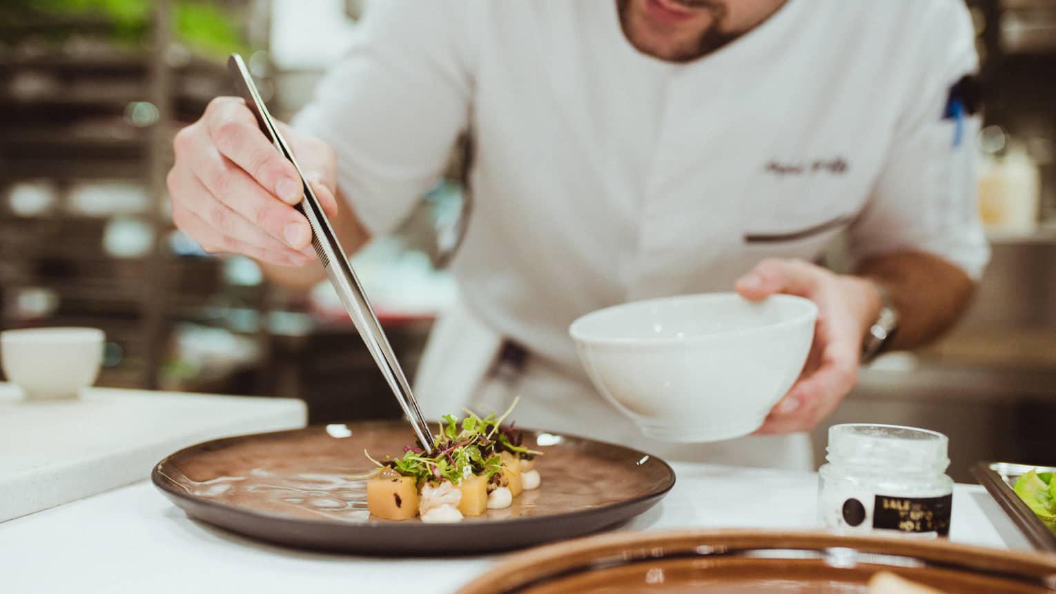 Chef holds long tweezers, places lettuce garnish on plate