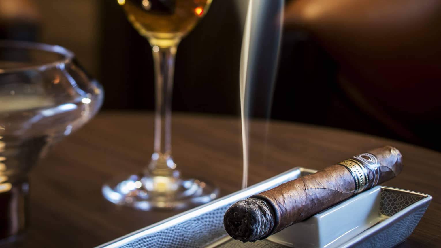 Smoking cigar on tray under glass with liquor