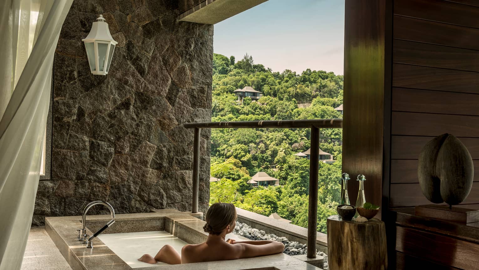 Back of woman sitting in rectangular hot tub, looking out open wall at mountain