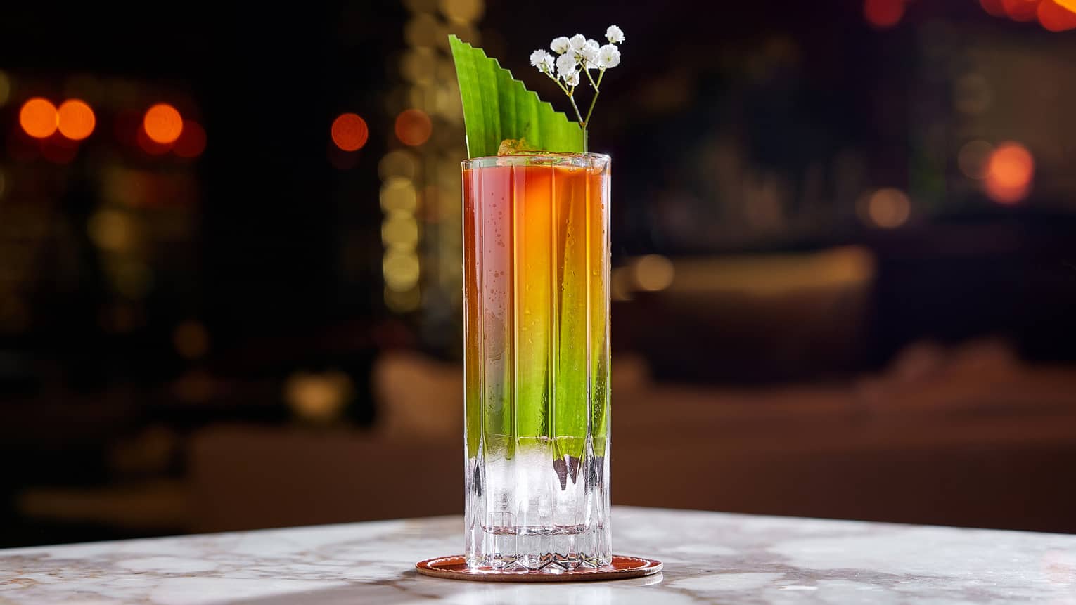 Red and green cocktail in highball glass with white flower garnish