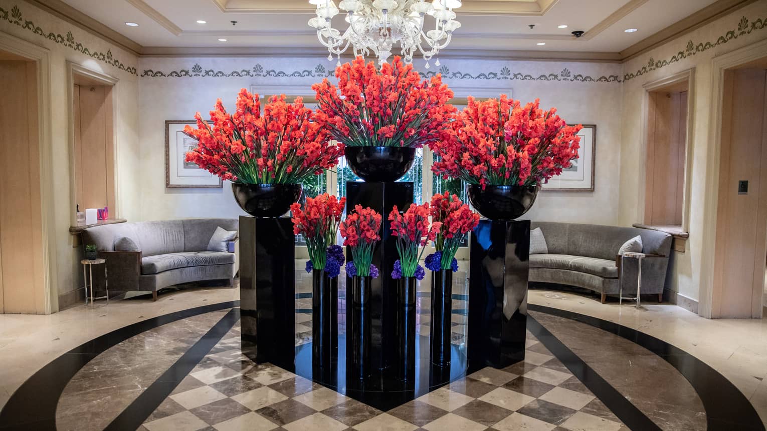 Hotel lobby, large red floral arrangements in black vases under crystal chandelier