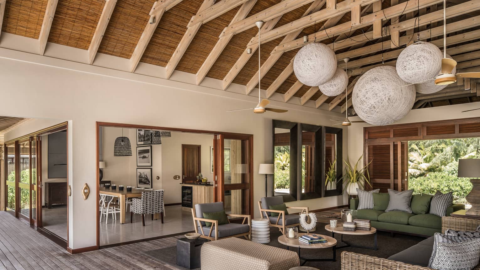 Large wicker globe chandeliers hang from beamed roof over open-air living room