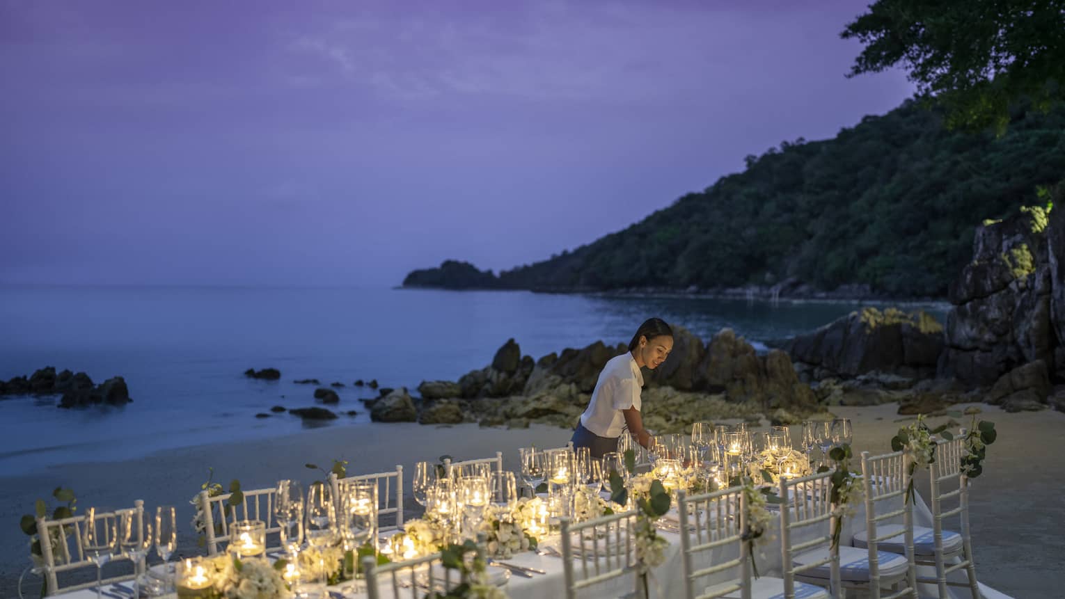 Team member sets up reception table on the beach at dusk