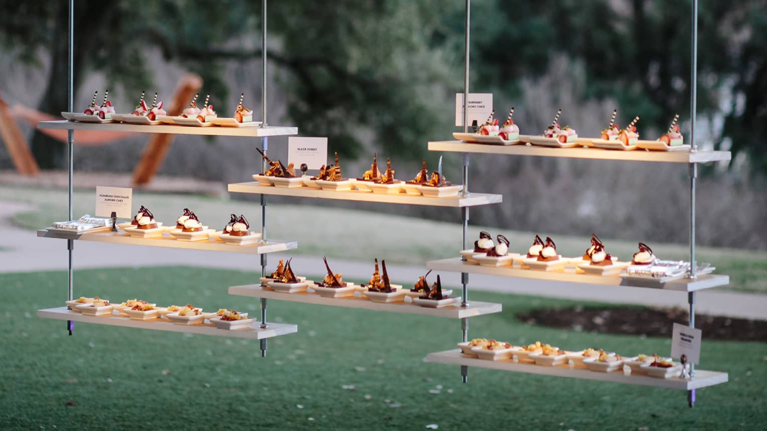 Trays holding hors d'oeuvres hang from trees in a courtyard 
