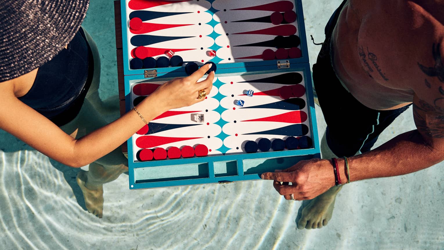 Aerial shot of man and woman in a pool, playing a floating game of backgammon
