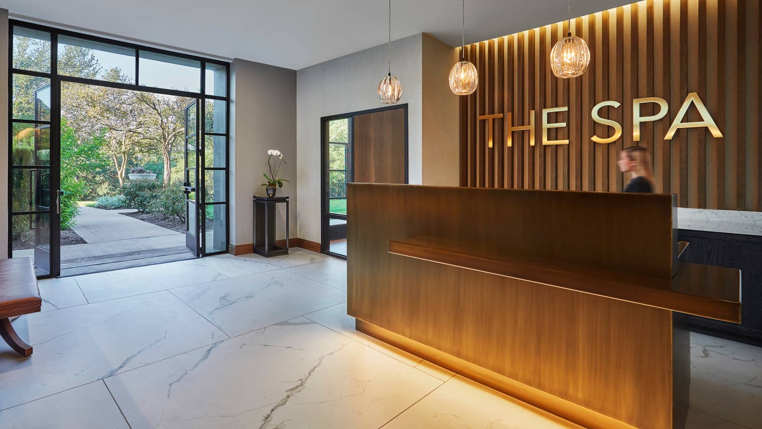 The Spa modern wood reception desk with gold sign, white marble floors, glass door