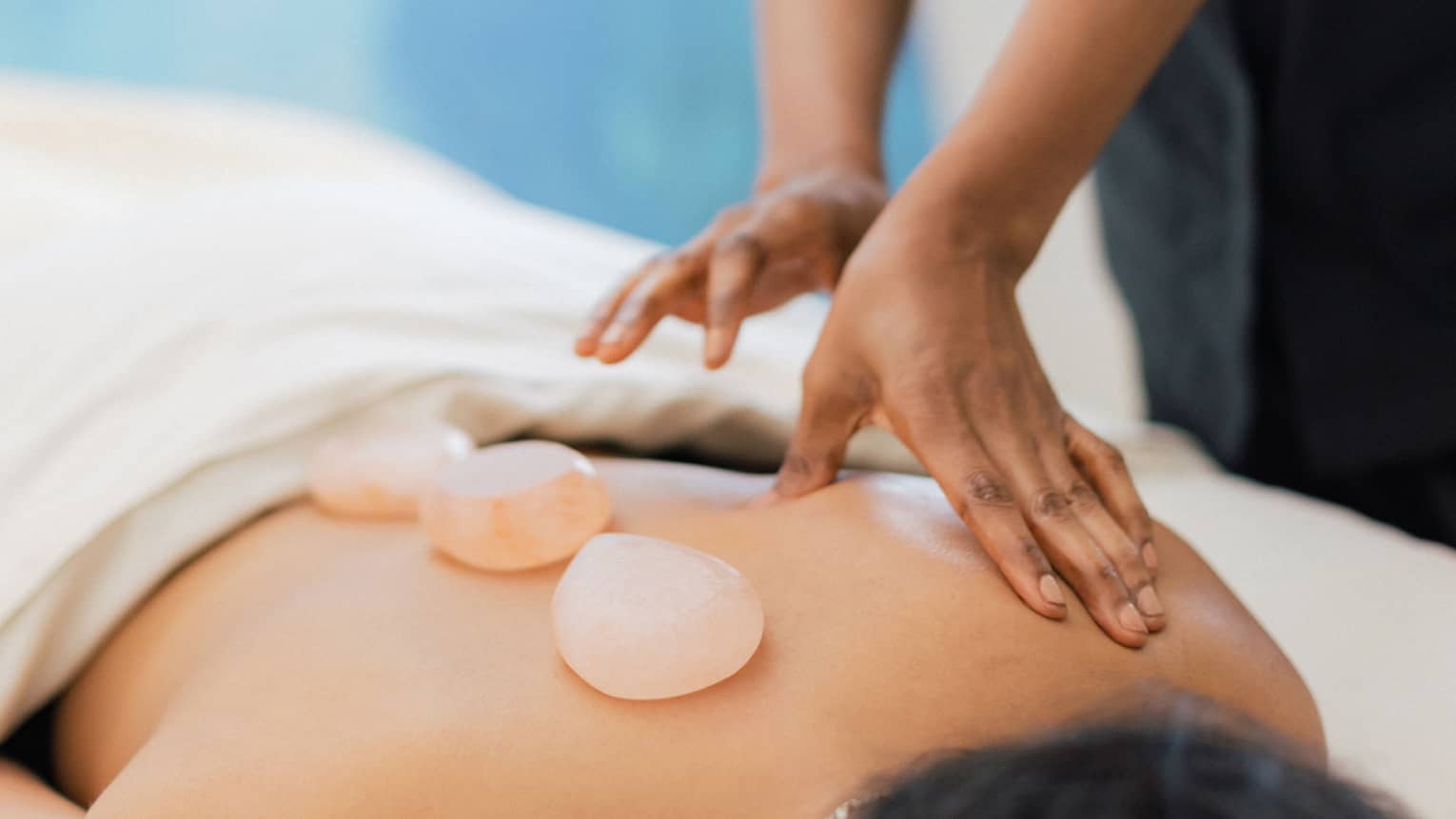 Masseuse places salt stones on a person's bare back