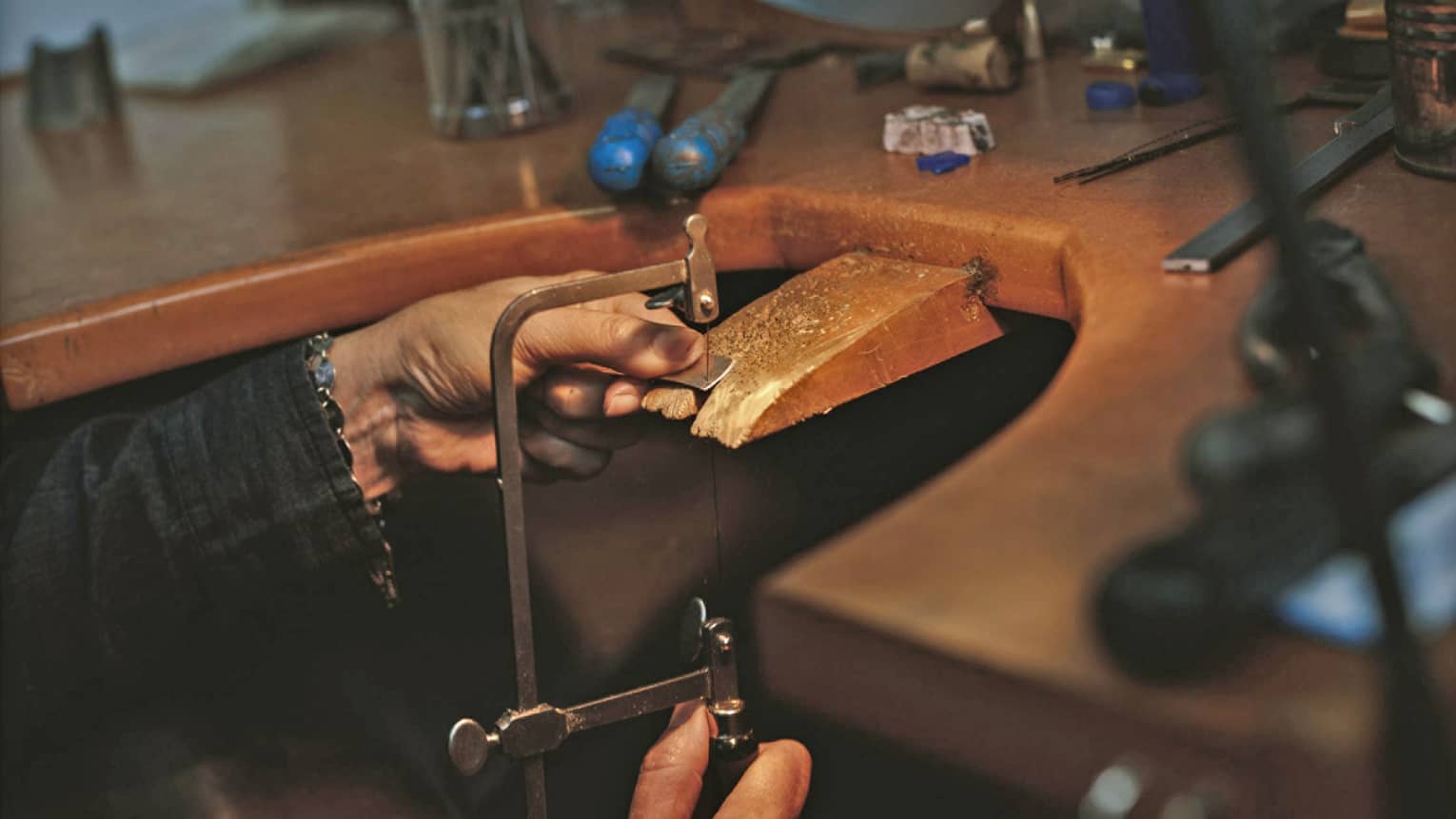 Jeweller's hands adjusting cutting tool to cut jewellery on wooden block