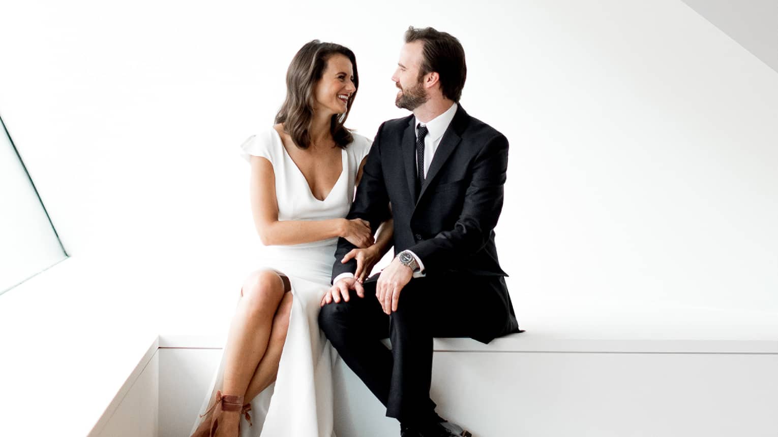 Bride and groom sit on ledge in bright, modern white room