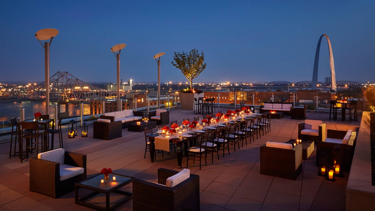 Aerial view of rooftop patio at night with lounge chairs and long communal dining table with candles