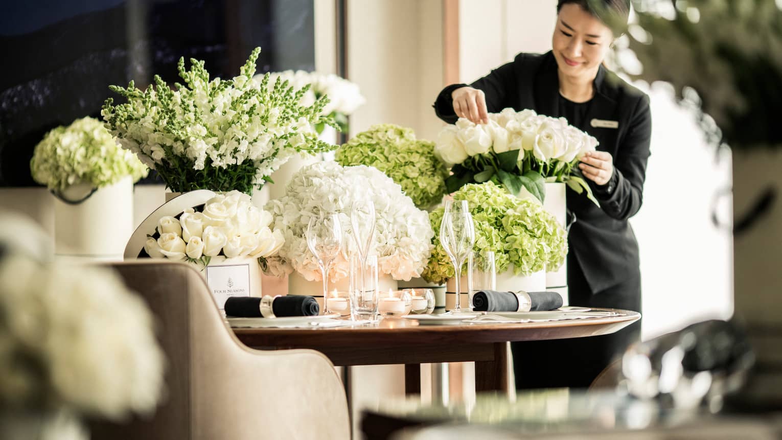 Hotel staff arranges white roses in vase on table with large vases, white flowers