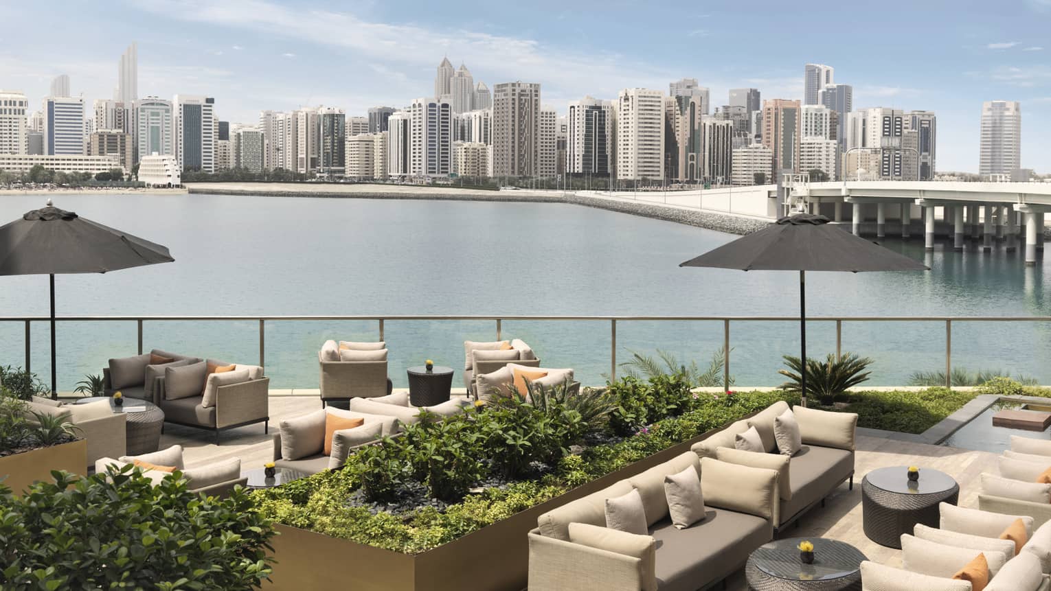 Outdoor sofas, umbrellas and planters on patio overlooking water, city