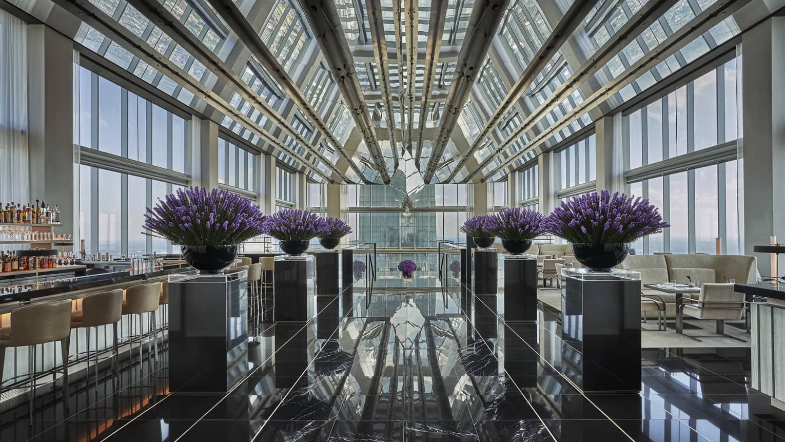Bar beside purple flowers in black planters, marble floor under glass loft penthouse ceiling