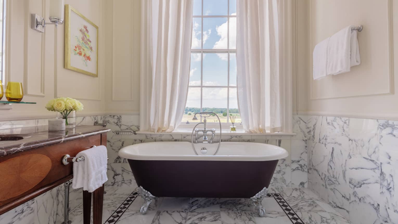 Bathroom with marble accents, large clawfoot tub, wooden vanity, window with white drapes