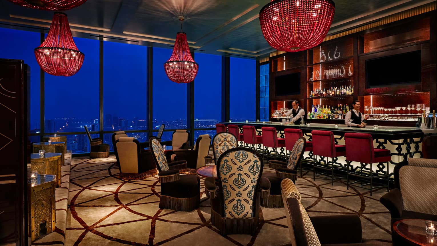 Dimly-lit Blue Moon lounge with large red beaded chandeliers, high-back plush chairs with decorative prints, bar
