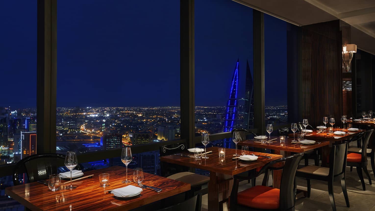 Re Asian Cuisine dining tables along floor-to-ceiling windows looking out at city lights at night