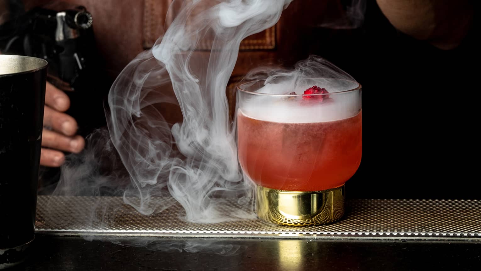 A red-coloured beverage with smoke from dry ice floating out of its glass