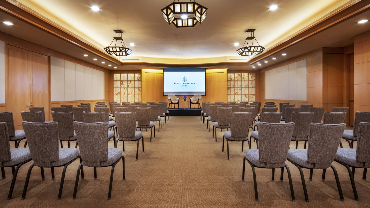 A wood-panelled function room with rows of chairs facing a presentation screen that shows a slide of the Four Seasons logo