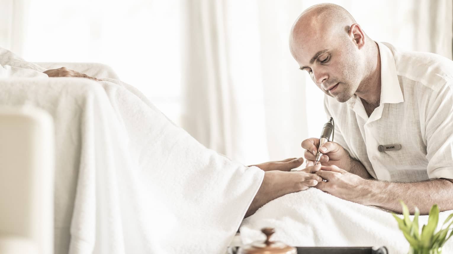 Man holds small pedicure tool at woman's feet in spa