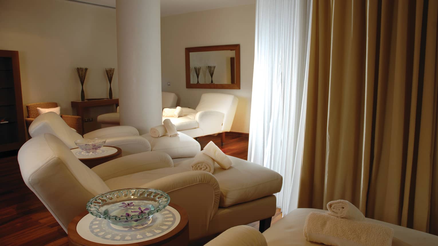 Three large plush chaise lounge sofas in dimly-lit spa room, rolled white towels