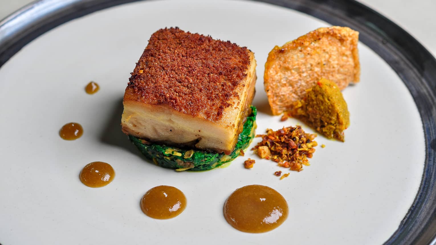 Babi Guling pork belly dish with crusted spice rub, sauteed pumpkin, dabs of orange sauce on white plate, 