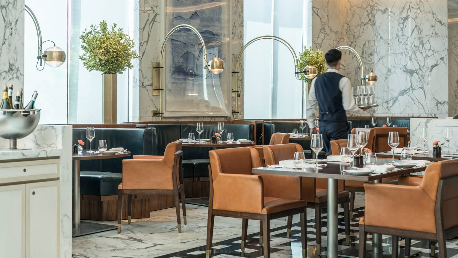 Server carries tray of glasses past lounge tables, chairs in Boccalino dining room