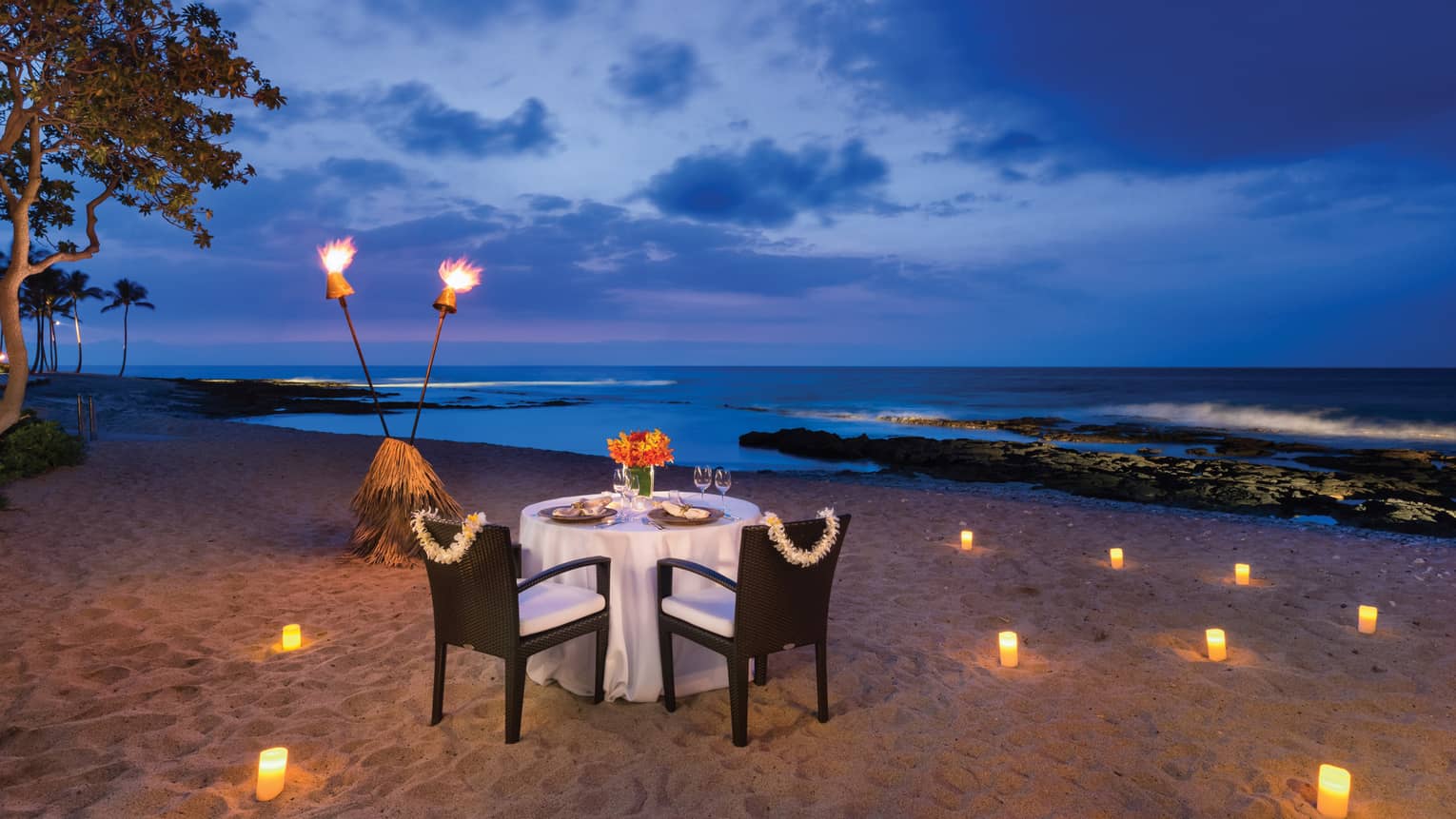 Couples dining table on sand beach with torches, glowing candles at night