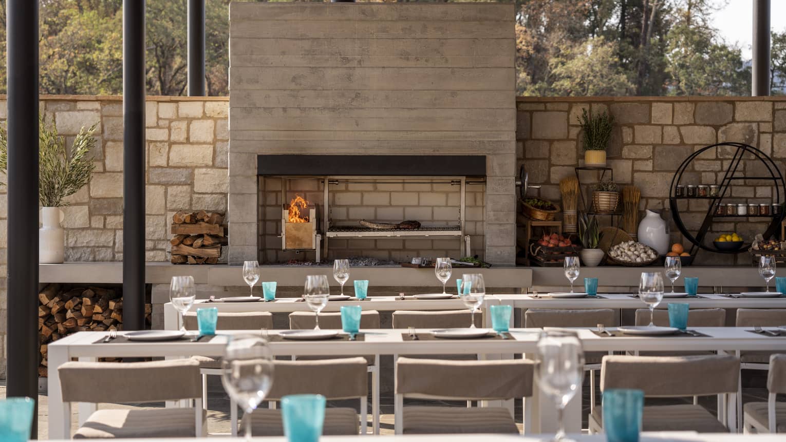 Rows of tables outside near a fire place and a stone wall.